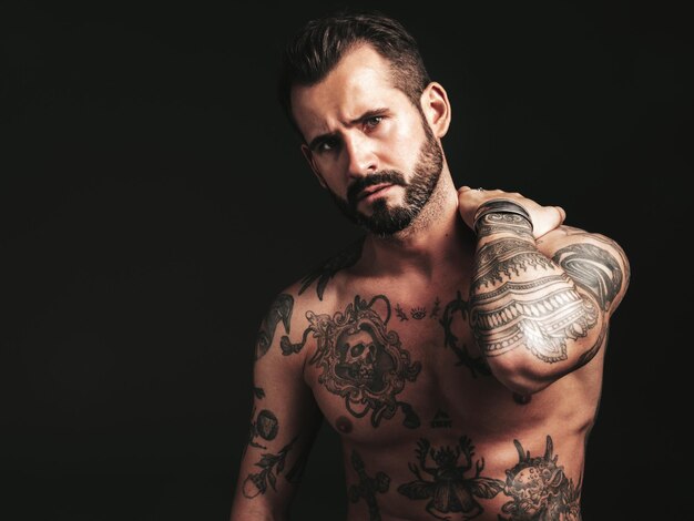 Portret van knappe zelfverzekerde stijlvolle hipster lamberseksueel model Sexy moderne man naakte torso met tattoosFashion mannelijke poseren in studio op donkere achtergrond