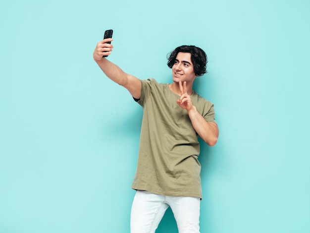 Portret van knappe zelfverzekerde stijlvolle hipster lamberseksueel modelMan gekleed in overmaat T-shirt en jeans Fashion man geïsoleerd in studio poseren in de buurt van blauwe muur