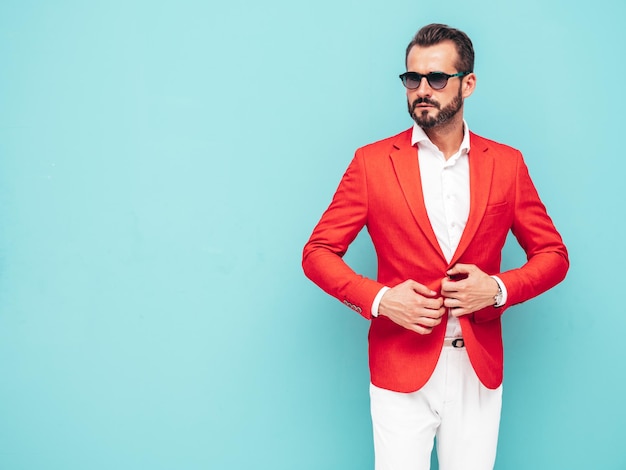 Portret van knappe zelfverzekerde stijlvolle hipster lamberseksueel modelSexy moderne man gekleed in elegant rood pak Fashion man poseren in studio in de buurt van blauwe muur in zonnebril