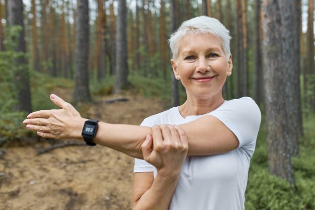 portret van kortharige gepensioneerde vrouw met whit t-shirt en slimme horloge om haar pols om de voortgang tijdens het hardlopen bij te houden