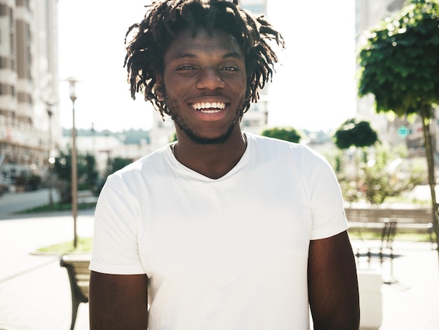 Portret van lachende knappe hipster modelOngeschoren Afrikaanse man gekleed in witte zomer tshirt en jeans Fashion man met dreadlocks kapsel poseren op de straat achtergrond