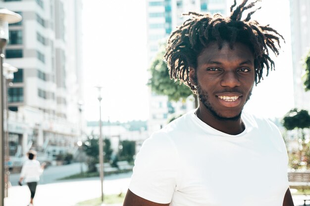 Portret van lachende knappe hipster modelOngeschoren Afrikaanse man gekleed in witte zomer tshirt en jeans Fashion man met dreadlocks kapsel poseren op de straat achtergrond
