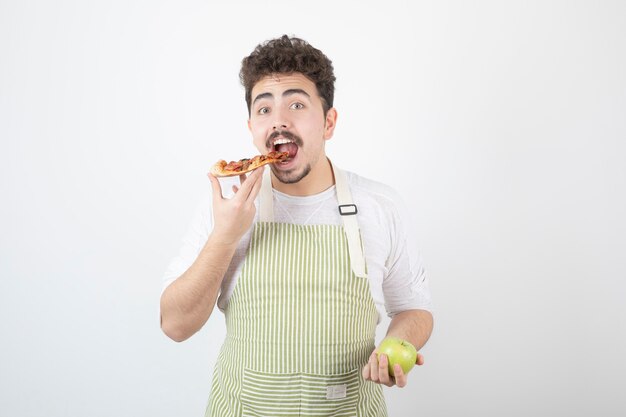 Portret van lachende mannelijke kok die pizza eet over appel op wit
