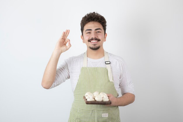 Portret van lachende mannelijke kok die rauwe champignons op wit houdt