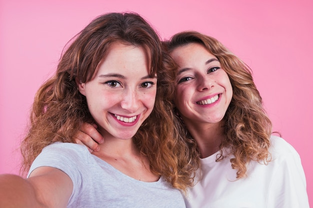 Gratis foto portret van lachende twee zussen tegen roze achtergrond