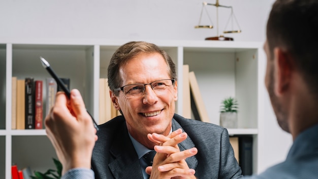 Portret van lachende volwassen advocaat zitten met zakelijke klant houden pen