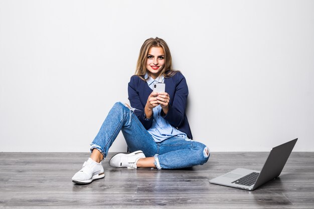 Portret van lachende vrouw tekstbericht typen of scrollen op internet met behulp van mobiele telefoon, zittend over grijze muur