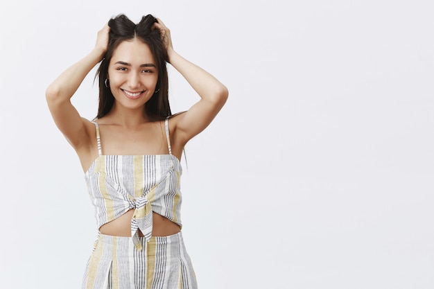 Portret van lachende zorgeloze en sensuele elegante vrouw in bijpassende kleding, haarlokken opheffen met handen en grijnzend, nieuwe kapsel leuk vinden en staren