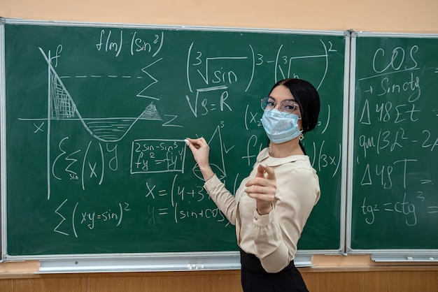 Portret van leraar met medisch masker tijdens coronavirusepidemie die tegen bord staat. educatieve wiskundeles