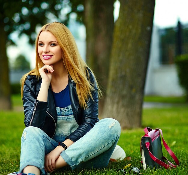 portret van leuke grappige blonde moderne sexy stedelijke jonge stijlvolle lachende vrouw meisje model in heldere moderne doek buiten zitten in het park in spijkerbroek met roze tas