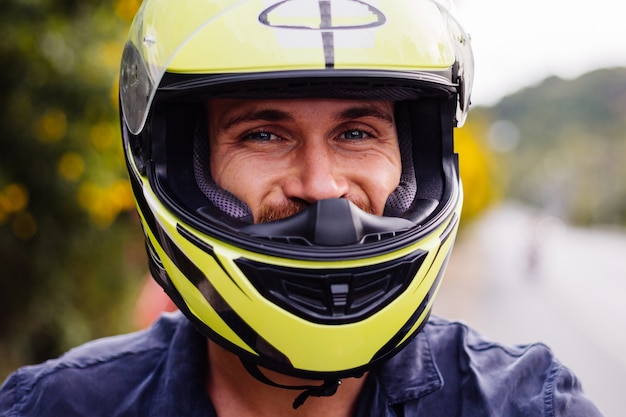 Portret van mannelijke fietser in gele helm op motor aan kant van drukke weg in Thailand