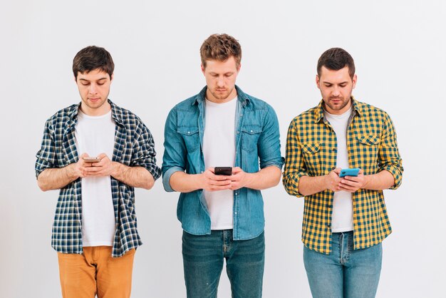 Portret van mannelijke vrienden die zich tegen witte achtergrond bevinden die mobiele telefoon met behulp van
