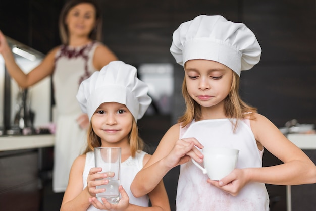 Portret van meisjes die de holdingsglas en kop van de chef-kokhoed dragen