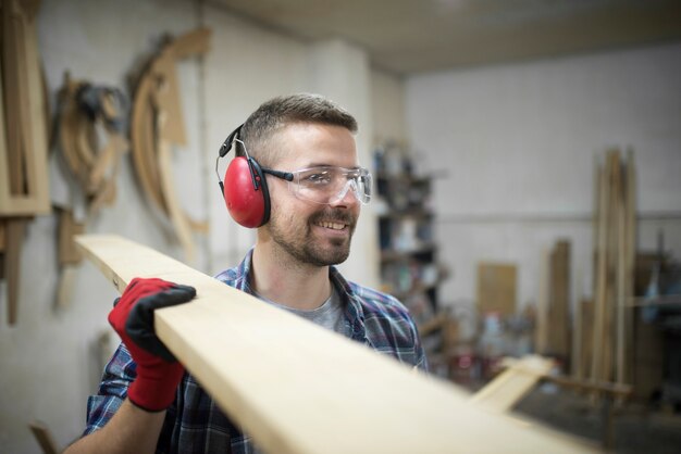 Portret van middelbare leeftijd blonde timmerman met ogen en oren bescherming houten plank uitvoering in houtbewerking timmerwerkplaats