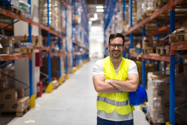 Portret van middelbare leeftijd magazijnmedewerker permanent in groot magazijn distributiecentrum met gekruiste armen