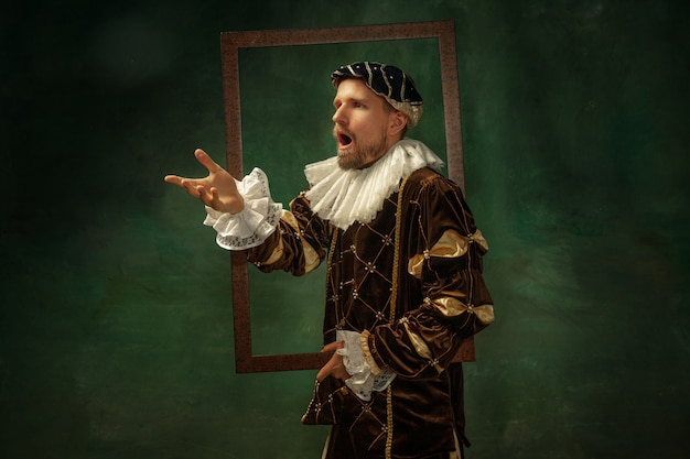 Portret van middeleeuwse jongeman in vintage kleding met houten frame op donkere muur