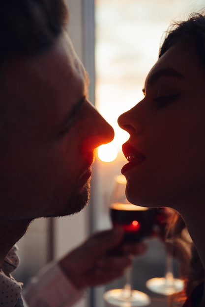 Portret van minnaars die bij zonsondergang kussen en glas met wijn thuis houden