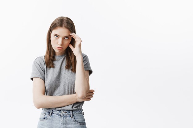 Portret van modieus jong Kaukasisch studentenmeisje dat met donker haar in modieuze uitrusting voorhoofd met hand masseert, kijkend opzij pissend van mamma die haar elementaire dingen onderwijst.