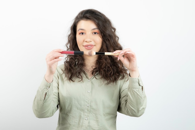 Portret van modieus meisje model bedrijf borstel met lippenstift over een witte muur.