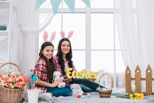 Portret van moeder en dochter zitten in de buurt van het venster met Pasen woord en bunny in de hand