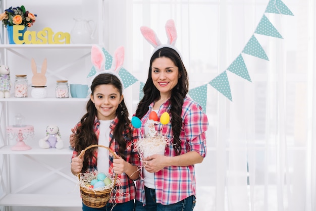 Portret van moeder en haar dochter met konijntjesoren die kleurrijke paaseieren in hand houden