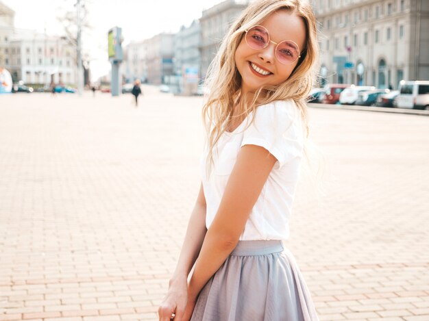 Portret van mooi glimlachend blond model gekleed in de zomer hipster kleren. Trendy meisje poseren in de straat in ronde zonnebril. Grappige en positieve vrouw die pret heeft