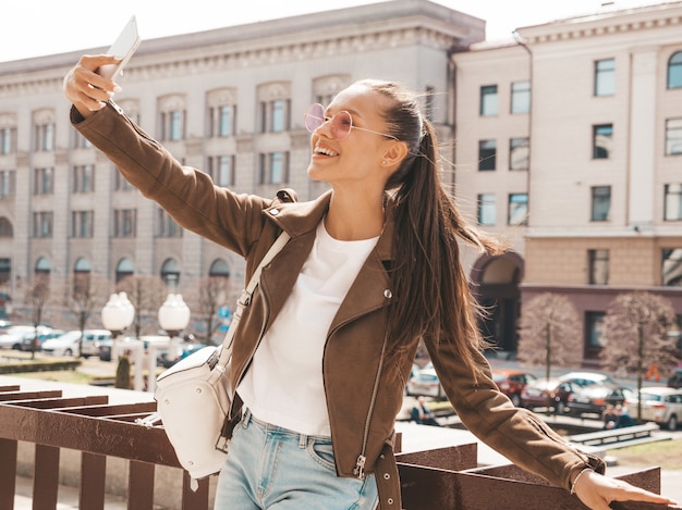 Portret van mooi glimlachend donkerbruin meisje in de zomer hipster jasje. Model nemen selfie op smartphone.