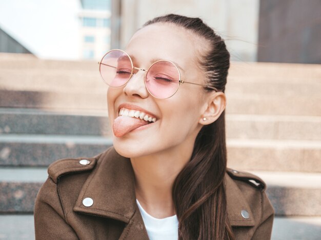 Portret van mooi glimlachend donkerbruin model gekleed in de kleren van het de zomer hipster jasje die haar tong tonen