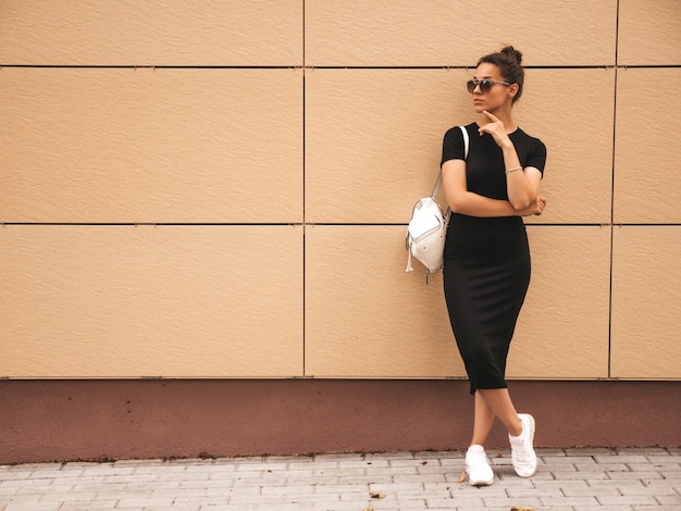 Portret van mooi glimlachend model gekleed in de zomerkleren. Trendy meisje poseren in de straat. Grappige en positieve vrouw die pret in zonnebril hebben