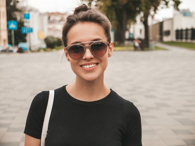 Portret van mooi glimlachend model gekleed in de zomerkleren. Trendy meisje poseren in de straat in zonnebril. Grappige en positieve vrouw die pret heeft