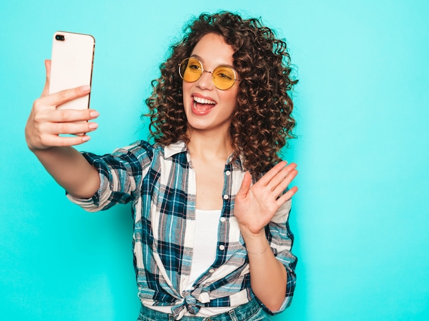 Portret van mooi glimlachend model met afro krullen kapsel gekleed in hipster zomerkleding. Trendy grappige en positieve vrouw maakt selfie