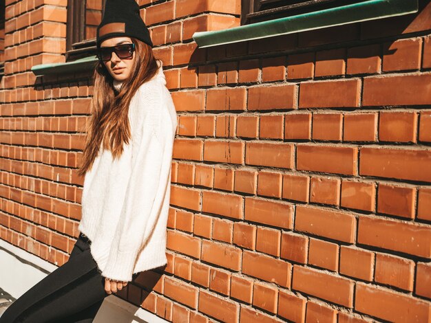 Portret van mooi lachend model. Vrouw gekleed in warme hipster witte trui en muts. Ze poseert op straat