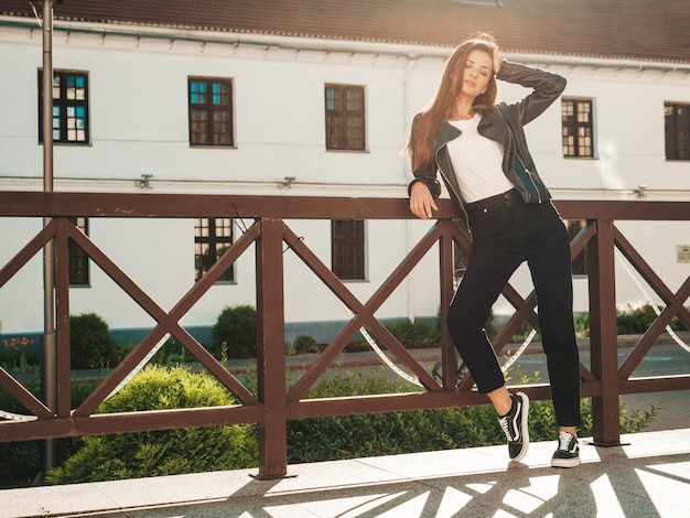 Portret van mooi lachend model. Vrouw gekleed in zomer hipster zwart leren jas en jeans. Trendy vrouw die zich voordeed op straat