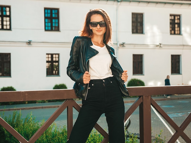 Portret van mooi lachend model. Vrouw gekleed in zomer hipster zwart leren jas en jeans. Ze poseert op straat