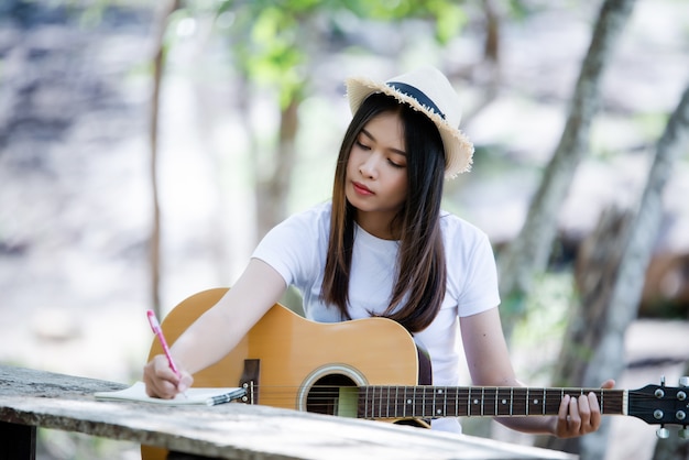 Portret van mooi meisje die de gitaar met het schrijven bij aard spelen