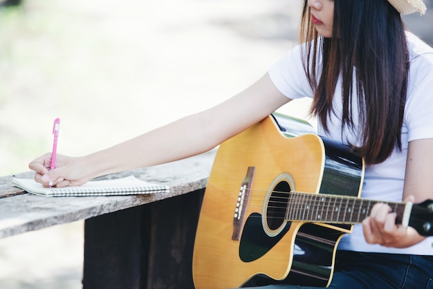 Portret van mooi meisje die de gitaar met het schrijven bij aard spelen