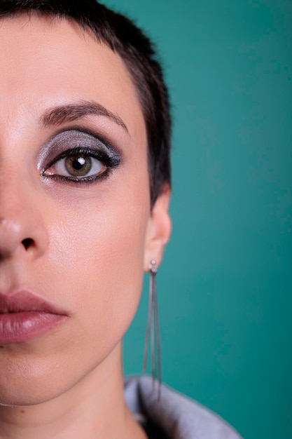 Portret van mooi model met de helft van het gezicht op de camera in de studio, met kort haar en prachtige make-up. Stijlvolle schattige vrouw die zich zelfverzekerd voelt poseren over geïsoleerde achtergrond