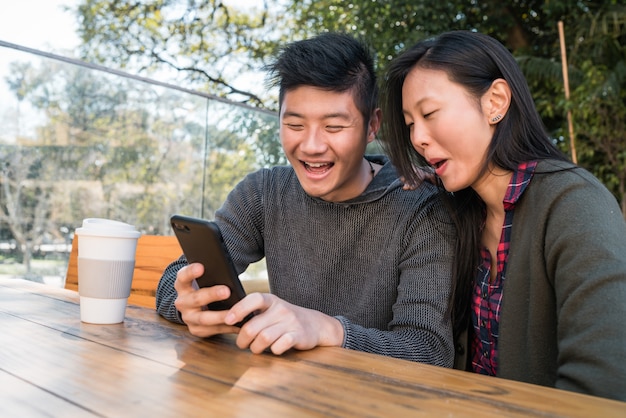 Portret van mooie Aziatische paar kijken naar de mobiele telefoon zittend en tijd doorbrengen in de coffeeshop.