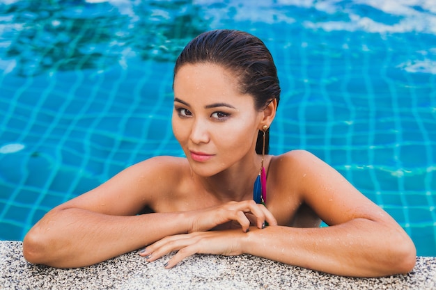 Portret van mooie Aziatische vrouw in zwarte zwembroek badend luxe spa zwembad dragen sylish veer oorbel glimlachend, sexy, slank gebruind lichaam en natte huid, zomer stijl accessoires,