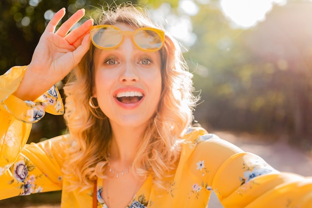 Portret van mooie blonde stijlvolle lachende vrouw in gele blouse dragen van een zonnebril selfie foto maken