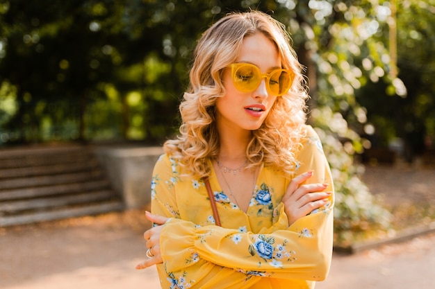 Portret van mooie blonde stijlvolle vrouw in gele blouse dragen van een zonnebril, kleurrijke zomer modetrend, zonnige dag