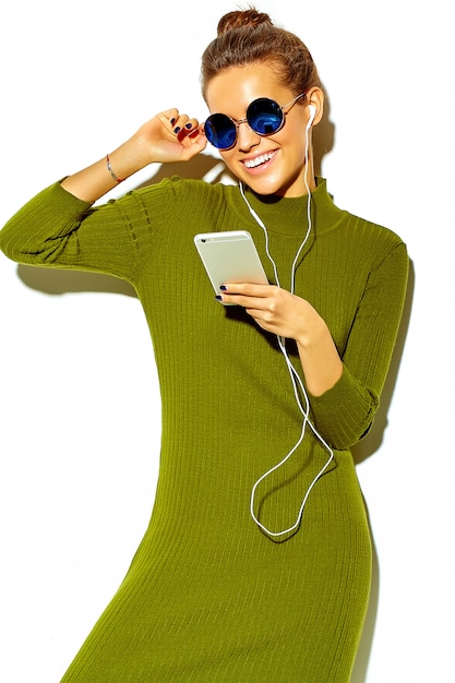 portret van mooie gelukkig schattige lachende brunette vrouw meisje in casual groene hipster zomer kleding geïsoleerd op wit in zonnebril luisteren muziek in smartphone met koptelefoon