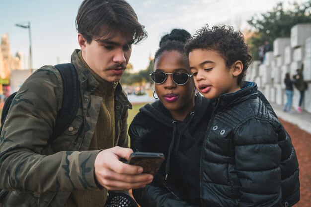 Portret van mooie gemengd ras etnische familie plezier, ontspannen en met behulp van mobiele telefoon in het park buiten.