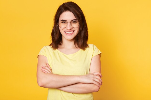 Portret van mooie glimlachende vrouw met gevouwen handen dat over gele studio wordt geïsoleerd
