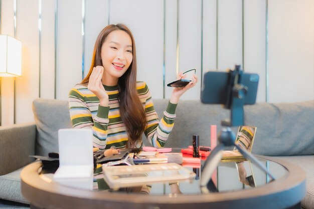 Portret van mooie jonge Aziatische vrouw beoordelingen en maakt gebruik van cosmetica op de bank