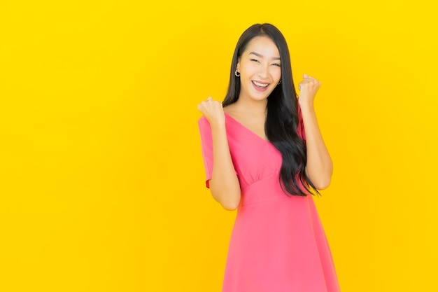 Portret van mooie jonge Aziatische vrouw glimlacht in roze jurk op gele muur