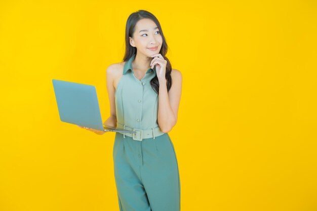 Portret van mooie jonge Aziatische vrouw glimlacht met computer laptop op geïsoleerde muur