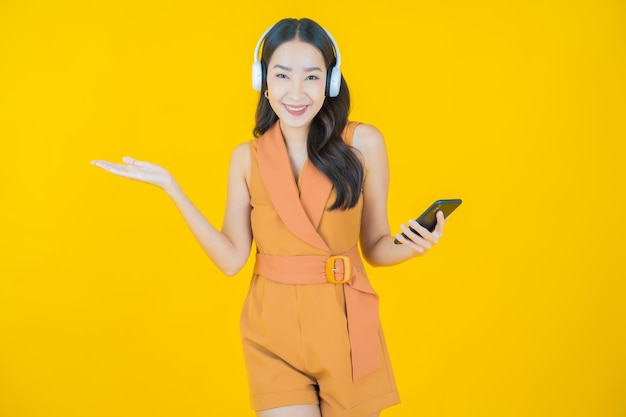 Portret van mooie jonge aziatische vrouw met hoofdtelefoon en smartphone om muziek te luisteren op gele achtergrond