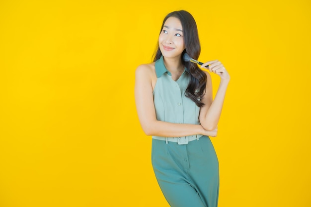 Portret van mooie jonge aziatische vrouw met make-up borstel cosmetica op gele muur