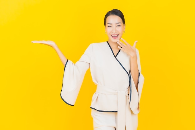 Portret van mooie jonge bedrijfs Aziatische vrouw die met wit kostuum op gele muur glimlacht
